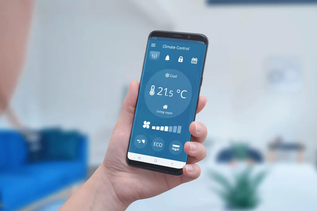 Main tenant un smartphone avec une application permettant le contrôle à distance du chauffage central, affichant la température de 21.5°C dans le salon